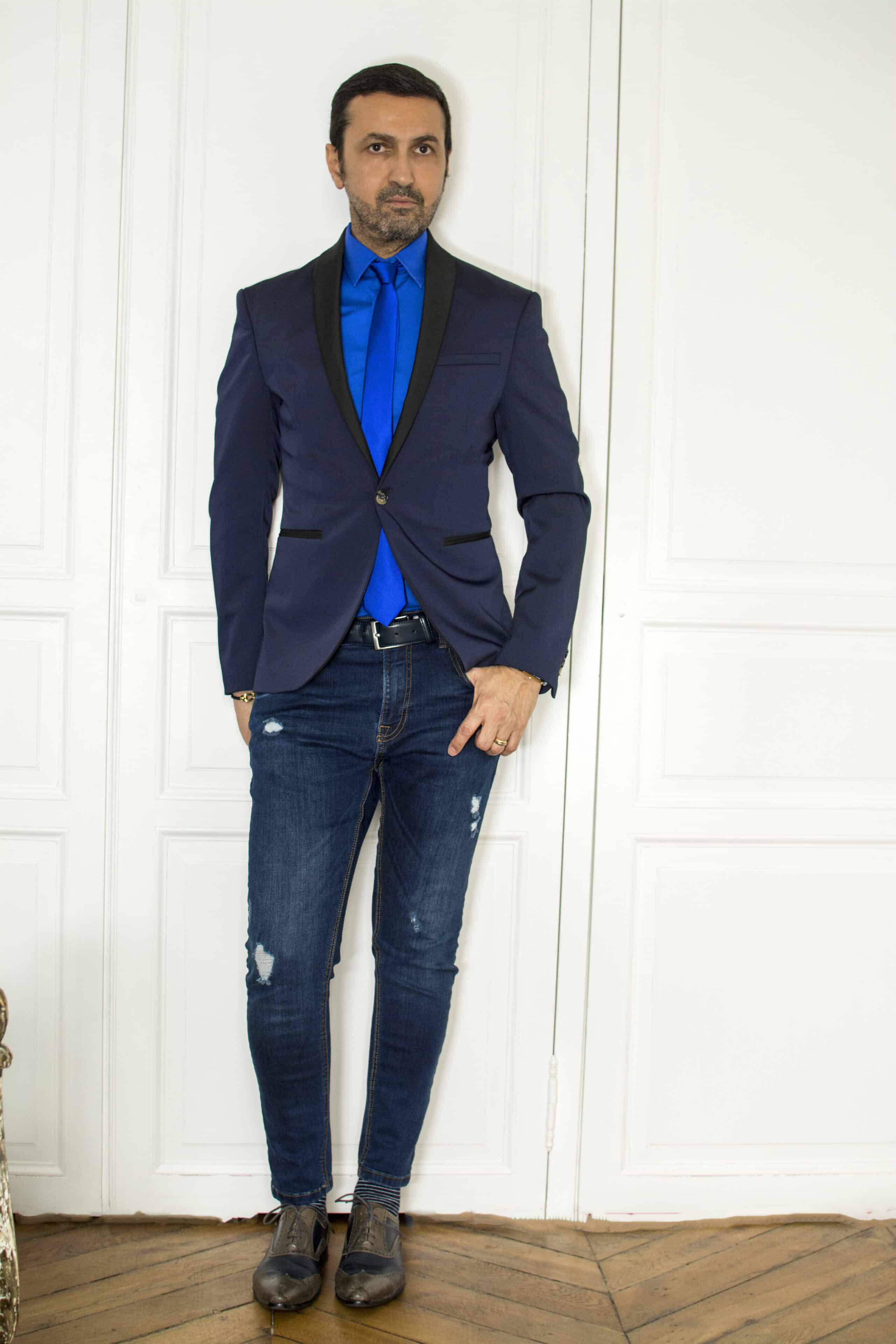 Il s’agit d’une tenue bleue monochrome pour homme, composée d’un jean bleu, d’une chemise bleu plus foncé, d’une cravate bleu dur et d’un blazer bleu moins foncé.