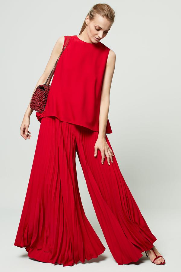 Top et pantalon en crêpe plissée d'un beau rouge accéssoirisée par un joli petit sac porté épaule de chez Carolina Herrera